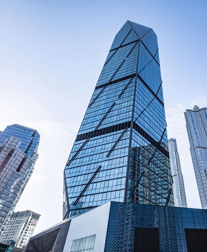 Tall modern skyscraper with blue glass facade, angled design, against a clear sky.