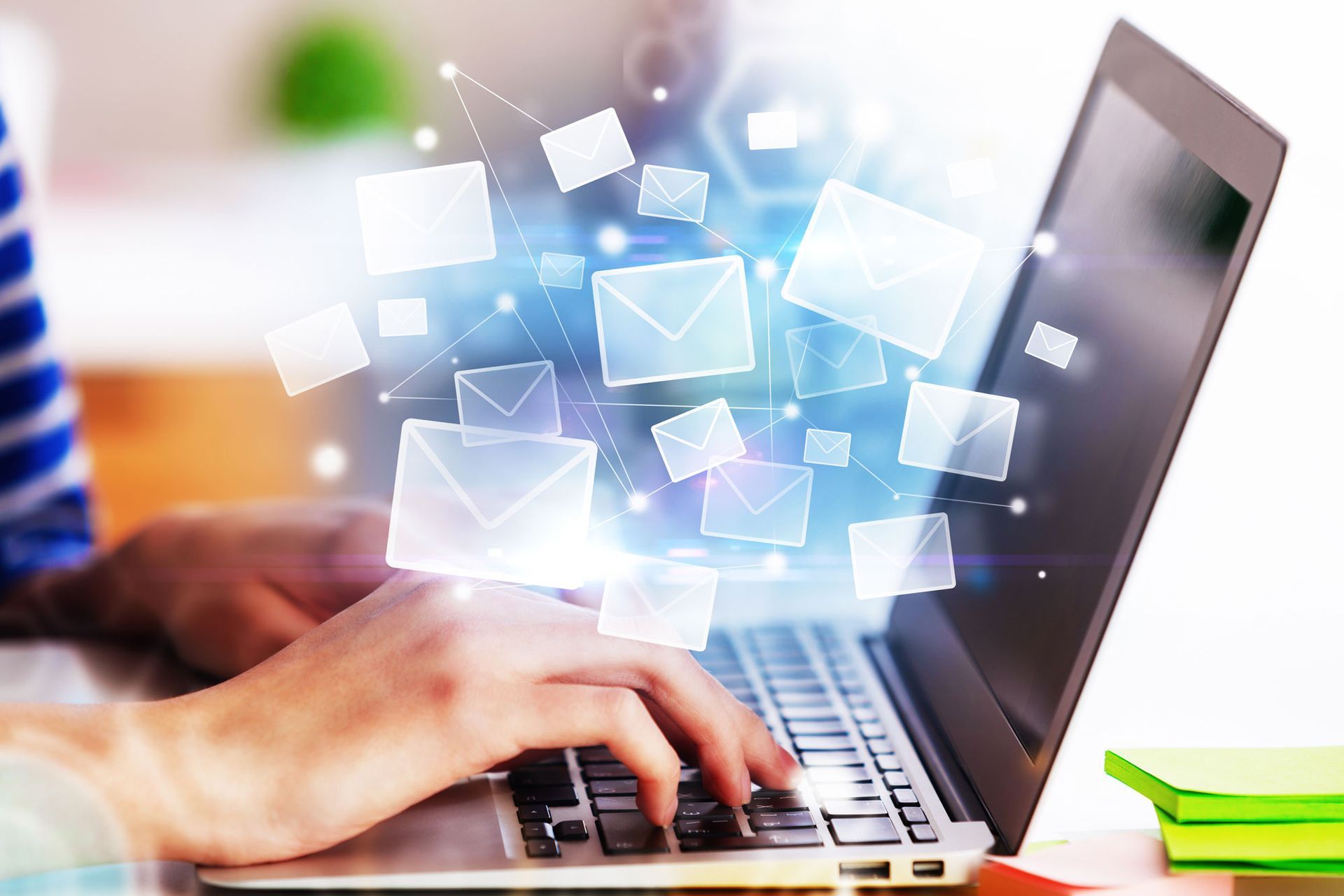 Person typing on laptop, glowing email icons radiating outward.