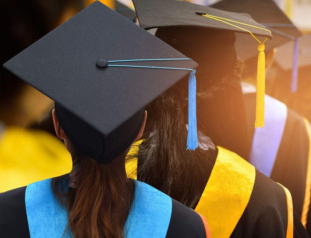 Graduates in caps and gowns, viewed from behind, with colorful stoles.