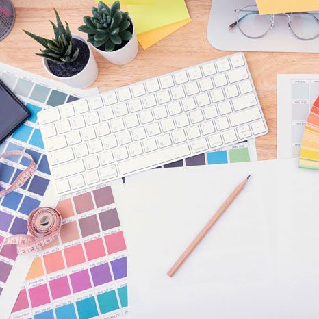Desk with keyboard, color swatches, pencil, tape measure, plants, and laptop.