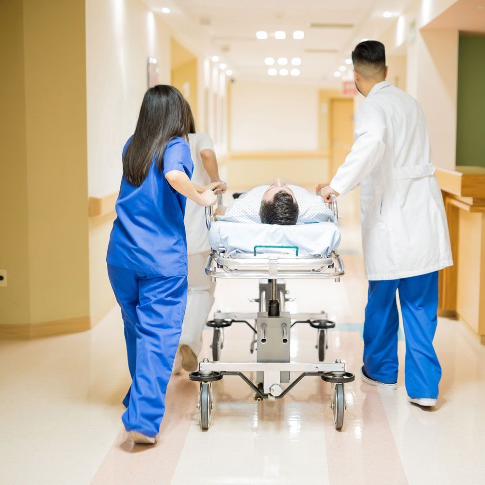 Medical staff pushing a patient on a stretcher down a hospital hallway.