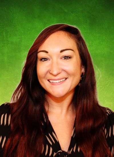 Woman with long, reddish-brown hair smiling, wearing a patterned blouse, set against a green background.