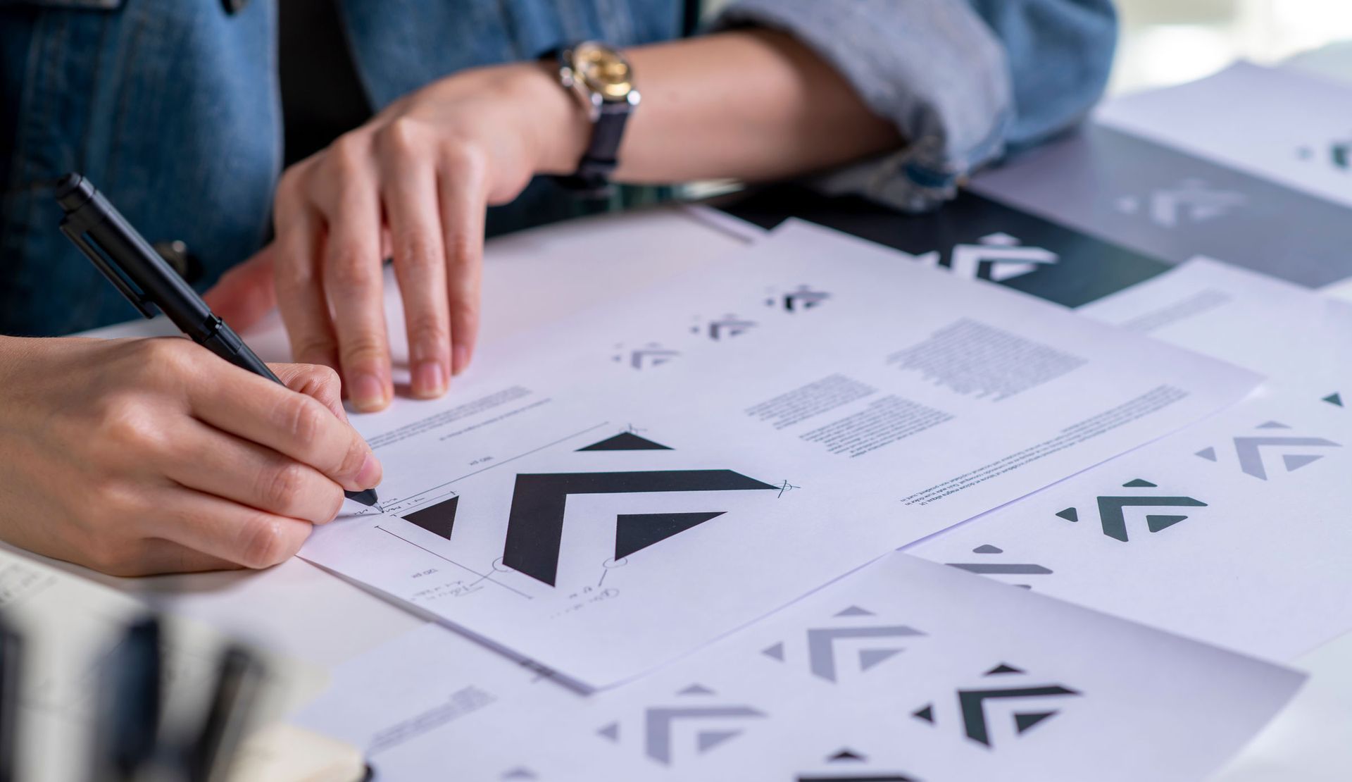 Person sketching logo designs on paper, focusing on geometric shapes and layouts.