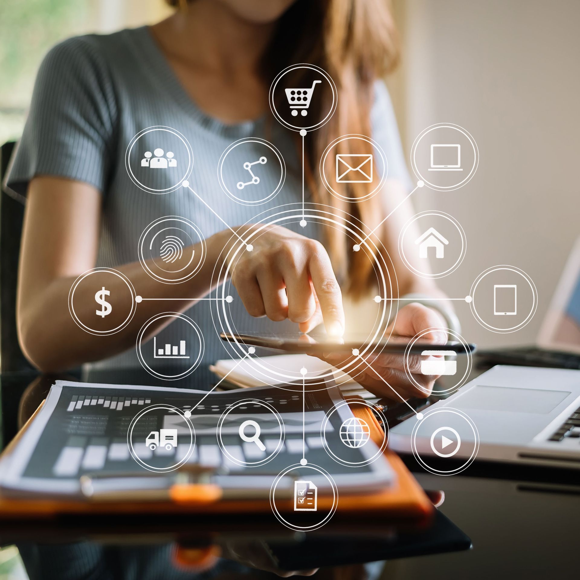 Woman uses tablet at a desk, surrounded by digital marketing icons. Laptop and graph on the desk.