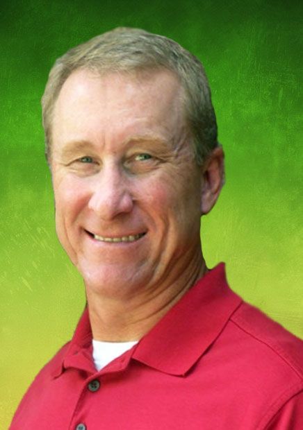 Man in red polo shirt smiles, posing in front of brick wall.