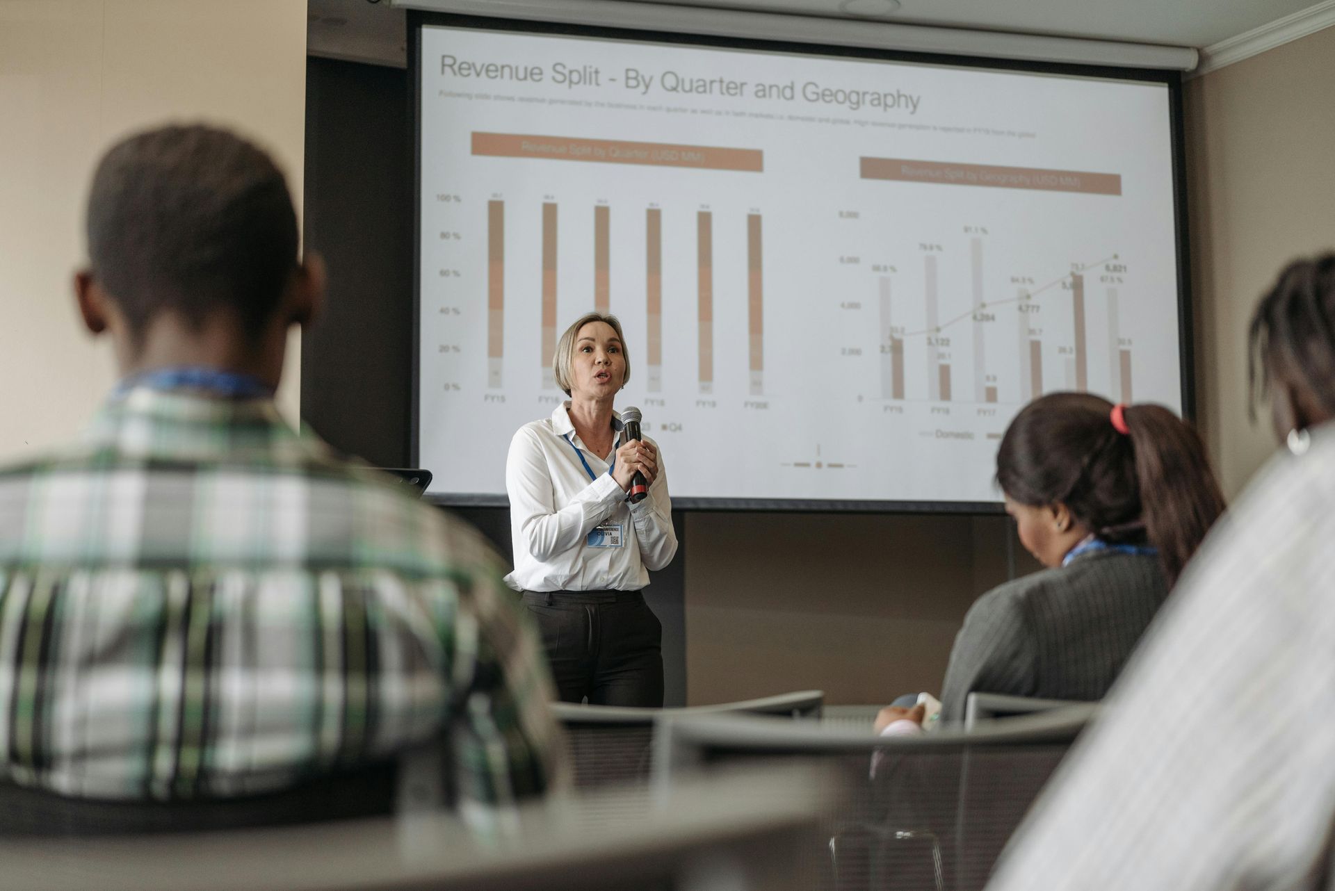 Woman standing at front of a room presenting about revenue to a room full of people