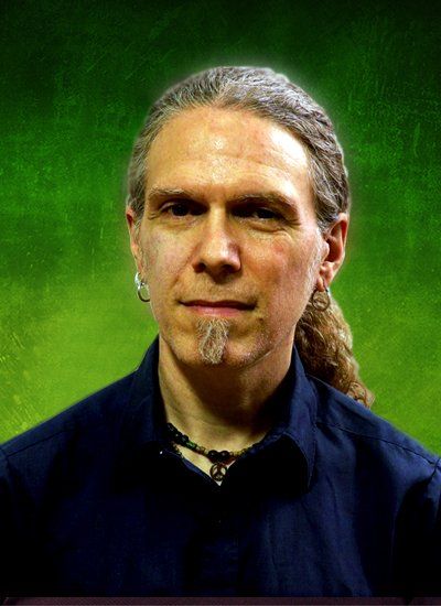 Man with long hair and goatee, wearing a dark blue shirt, against a green background.