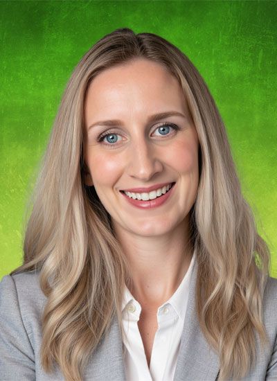 Woman with blonde hair, smiling, wearing a grey blazer, white shirt, and standing in front of a green gradient background.