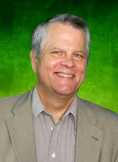 Man in light jacket smiles, green backdrop.