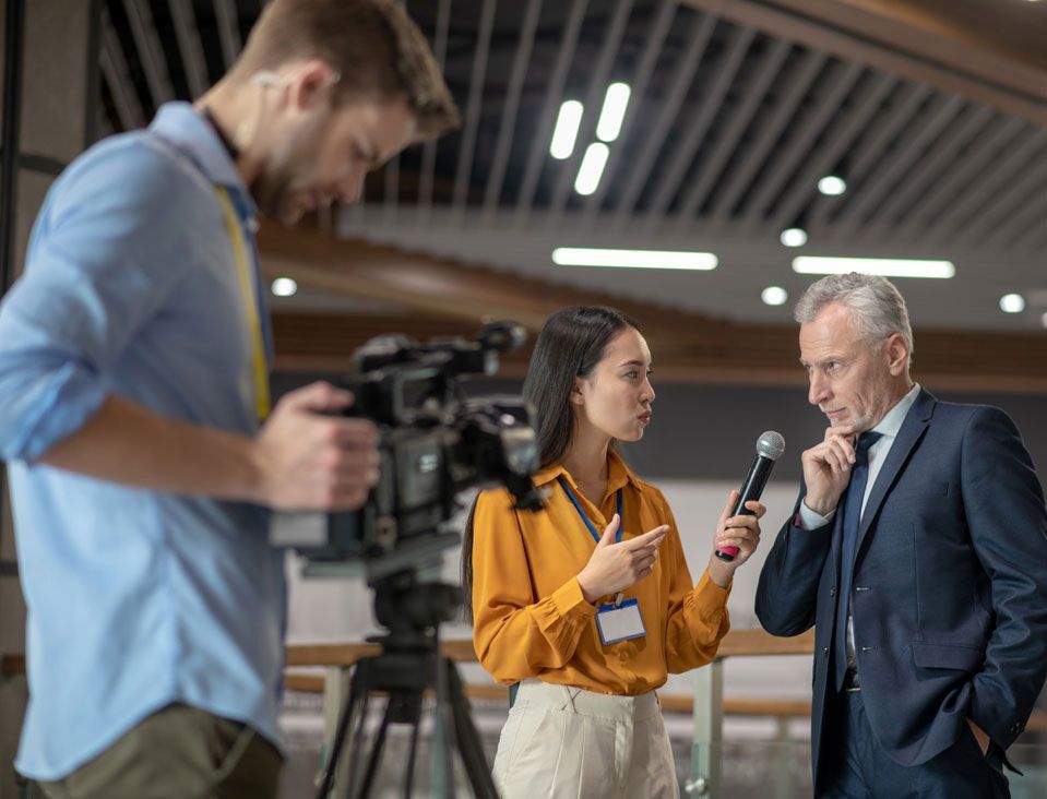 A journalist interviews a man with a microphone, while a cameraman films them.