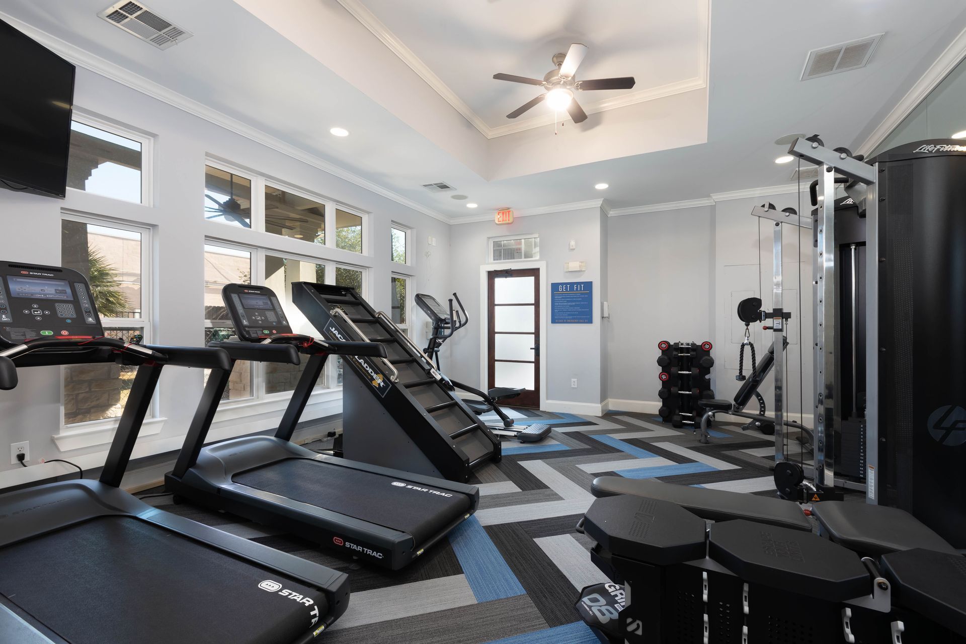 A gym with treadmills , exercise bikes , and a ceiling fan.