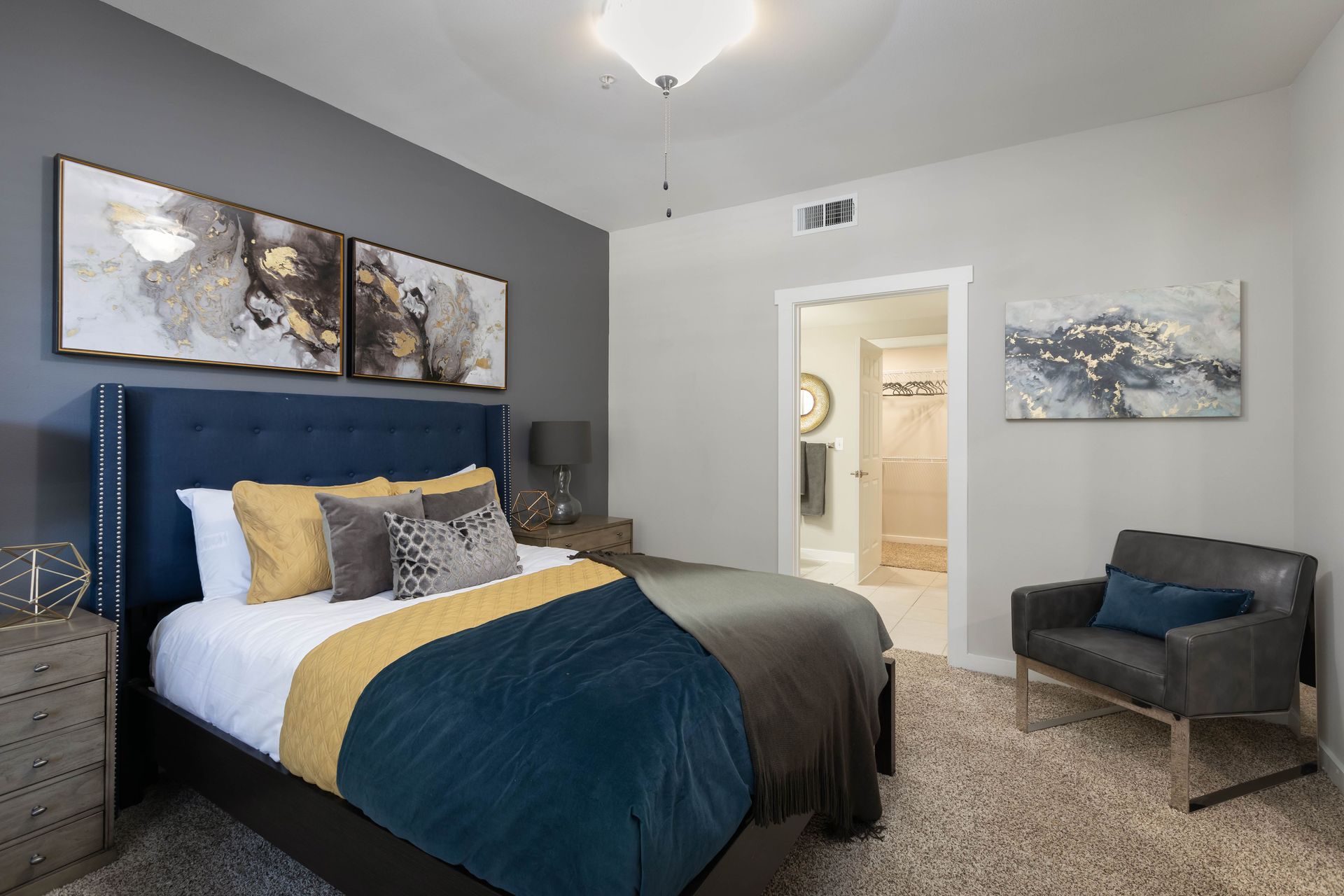 A bedroom with a bed , chair , nightstand and paintings on the wall.