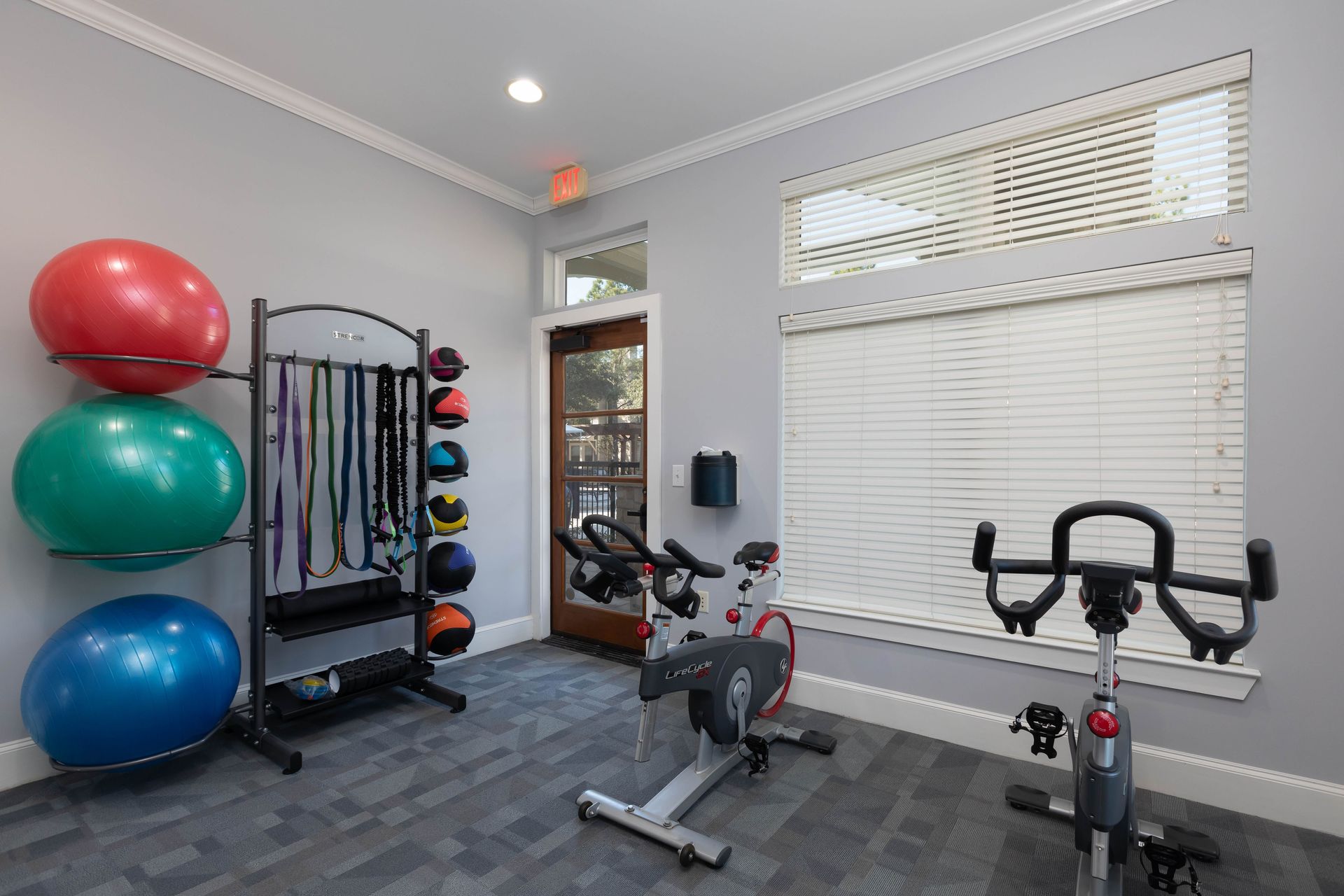 A gym with a bicycle , exercise balls , and a window.