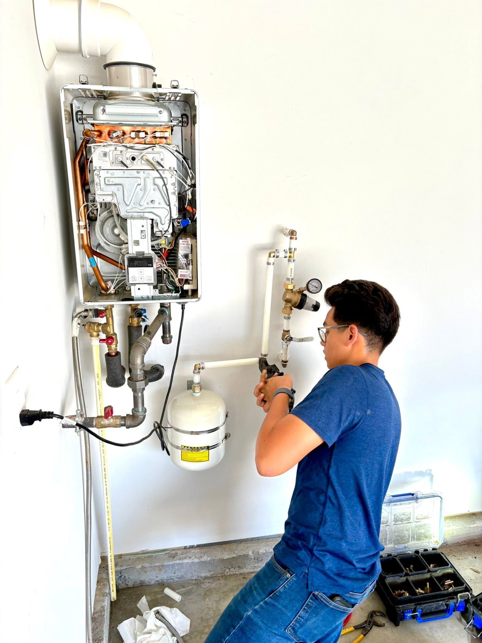 Technician installing a wall-mounted water heater in a utility room, holding a pipe wrench.