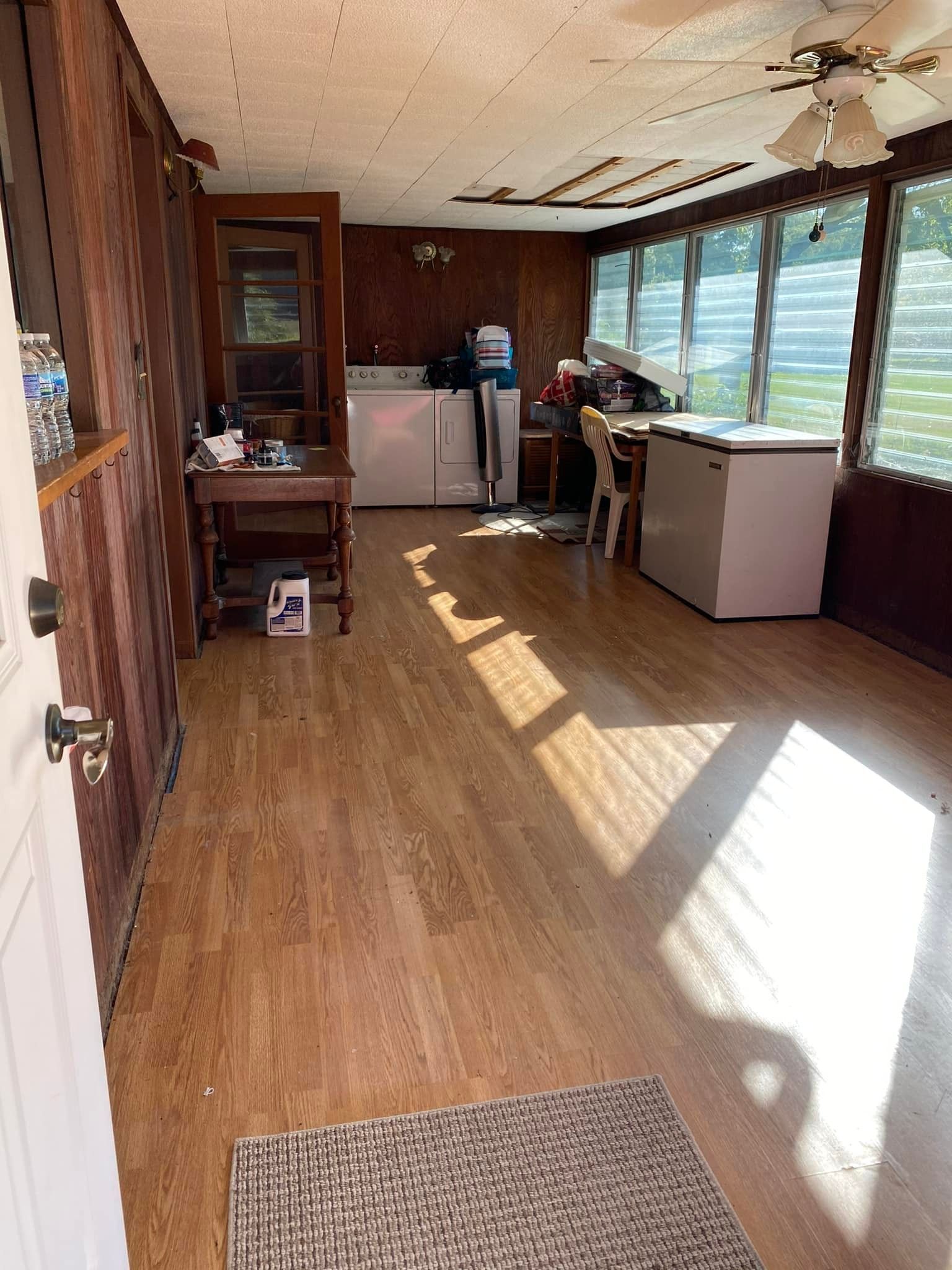 Sunroom with wood paneling, appliances, freezer, and a person standing.