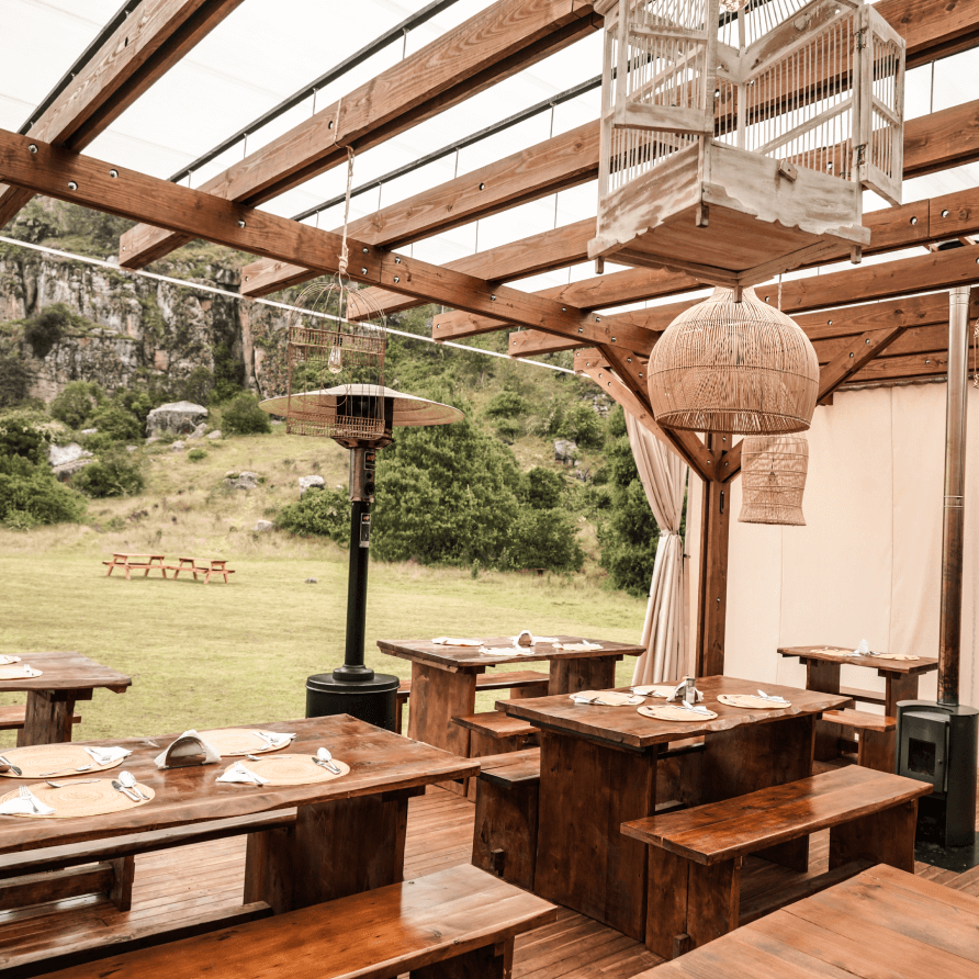 Un restaurante con mesas y bancos de madera bajo una pérgola de madera.