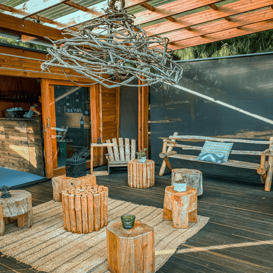 Una terraza de madera con taburetes, un banco y una lámpara de araña.