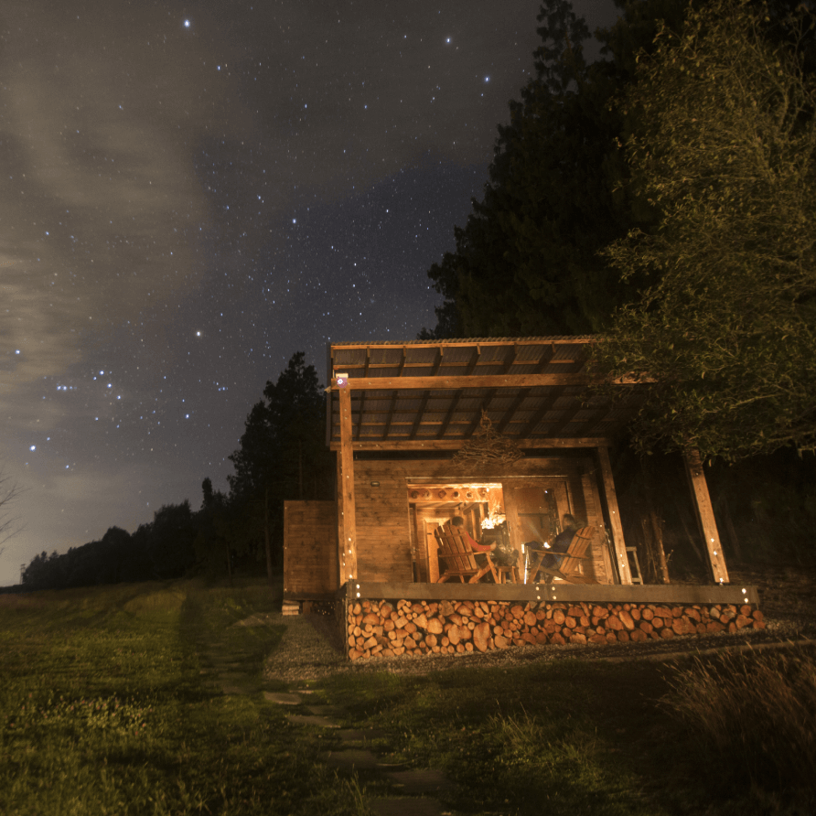 Una pequeña casa de madera con un porche cubierto se ilumina por la noche