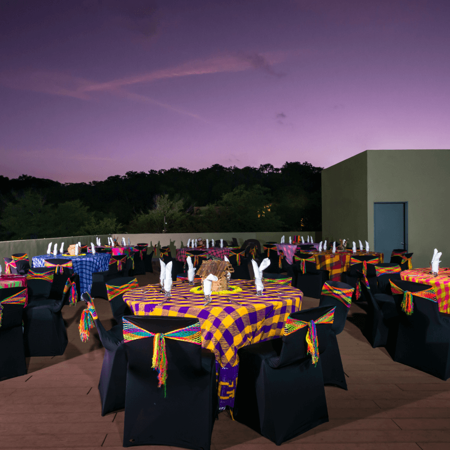 Mesas y sillas preparadas para una fiesta con un cielo morado de fondo.