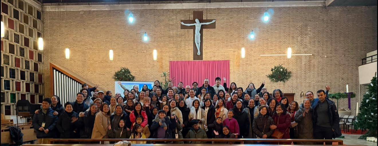 Large group of people pose in front of a church altar with a crucifix, some raising hands.