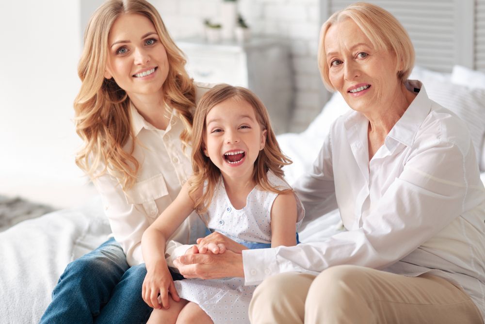 A mother , daughter and grandmother are sitting on a bed.