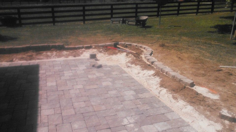 A brick patio is being built in a backyard with a fence in the background.
