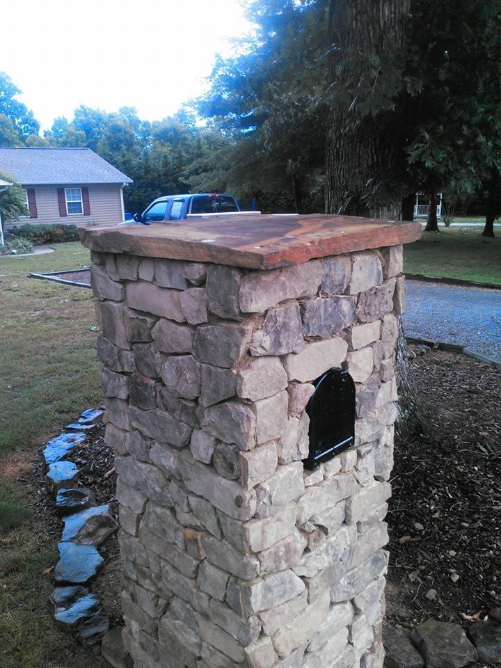 A stone post with a mailbox on it in front of a house