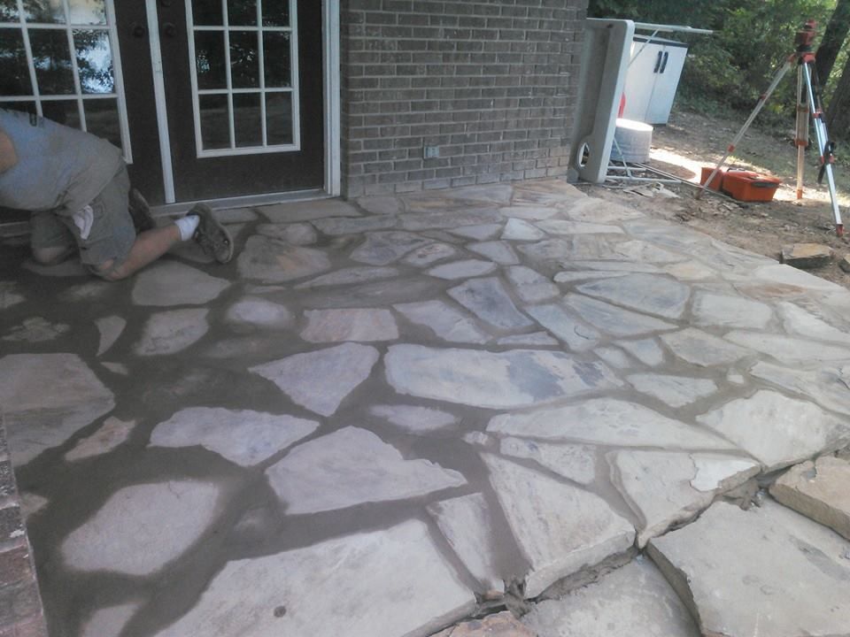 A man is kneeling on a stone patio in front of a brick building