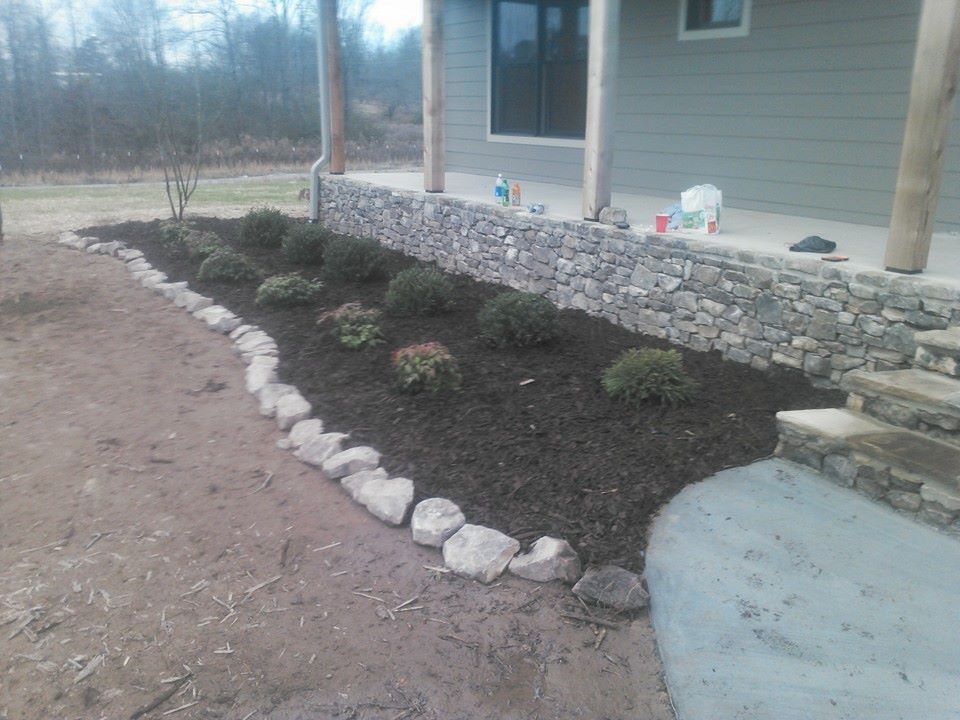 A stone wall surrounds a lush green garden in front of a house.