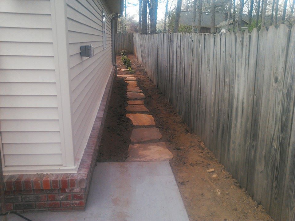A sidewalk leading to a house next to a wooden fence.