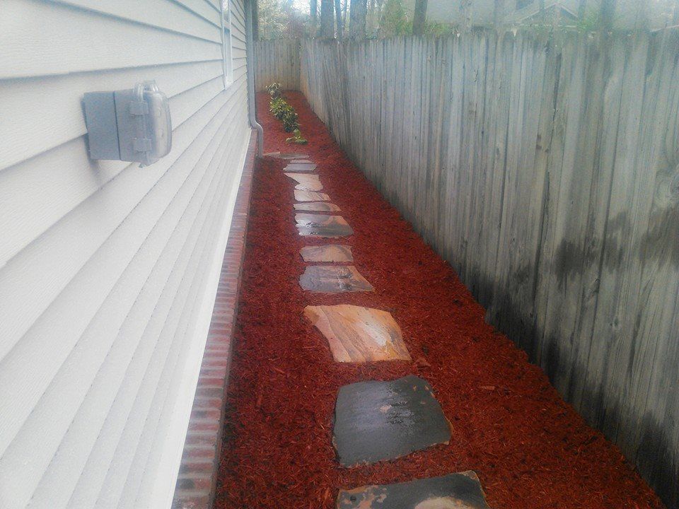 A sidewalk with stepping stones and red mulch next to a house.