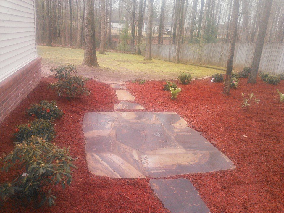 A stone walkway leading to a house surrounded by red mulch.