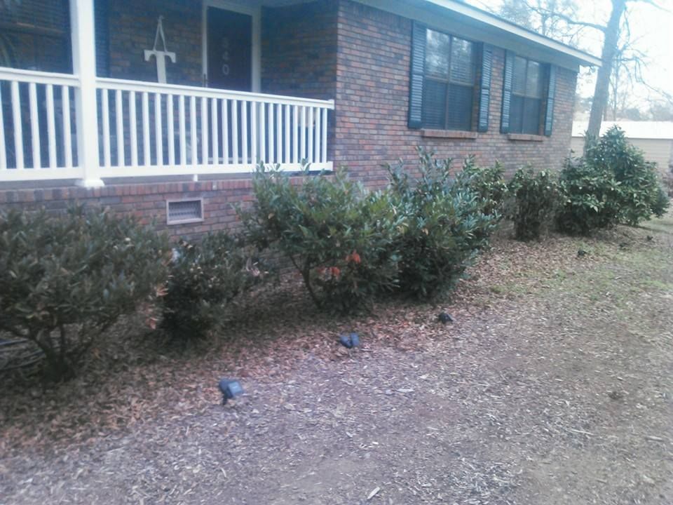 A brick house with a porch and bushes in front of it.