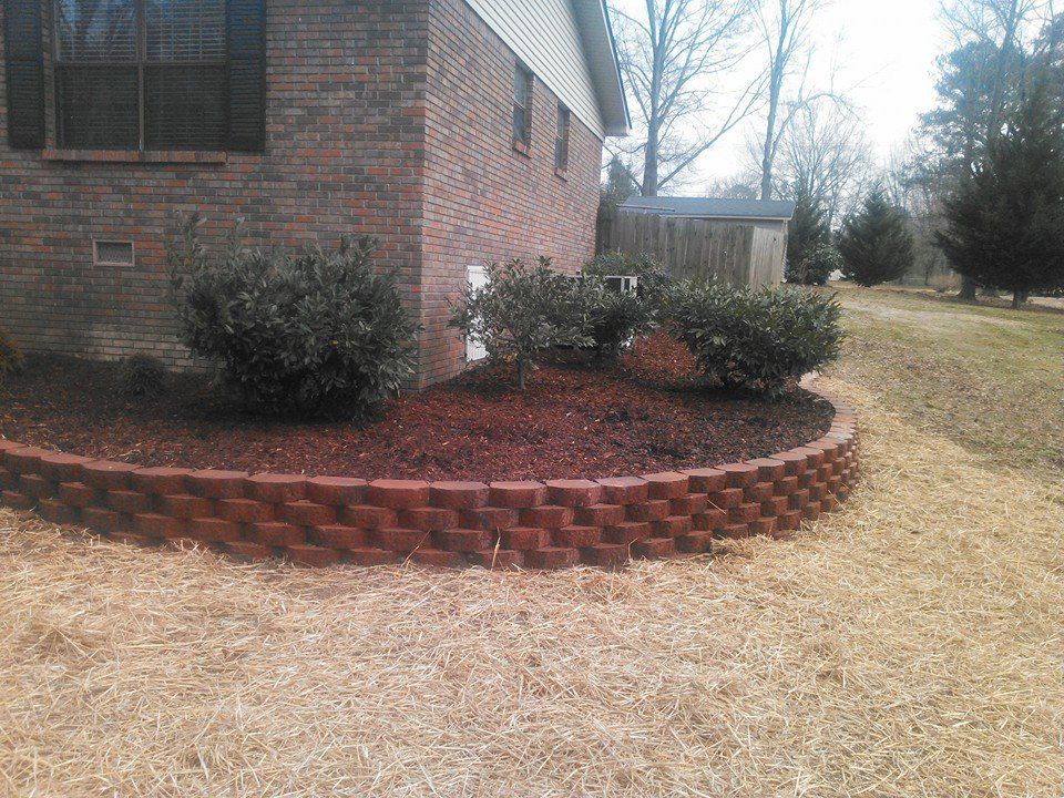 A brick wall surrounds a garden in front of a brick house.
