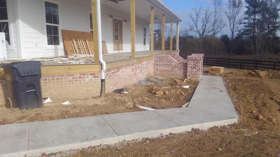 A white house with a brick porch and a concrete walkway leading to it.