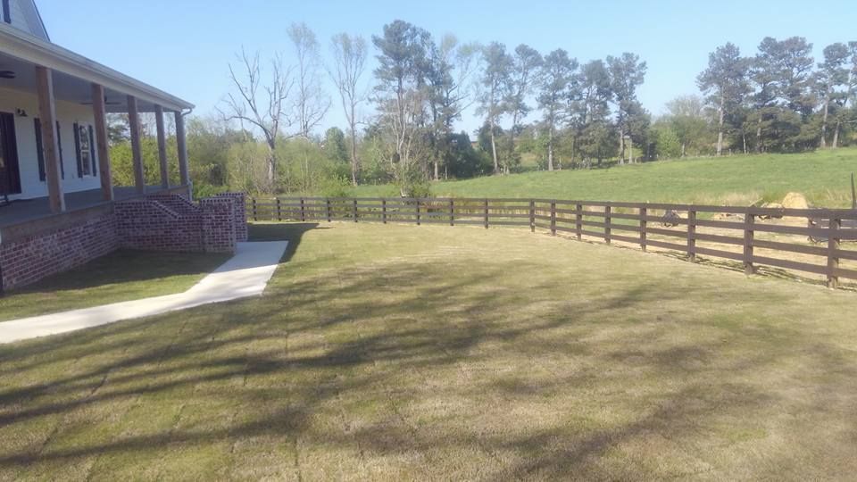 A large lawn with a wooden fence in front of a house.