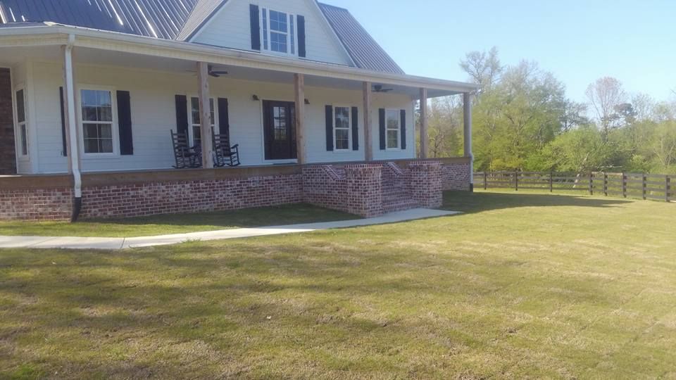 A white house with a porch and a large lawn in front of it.