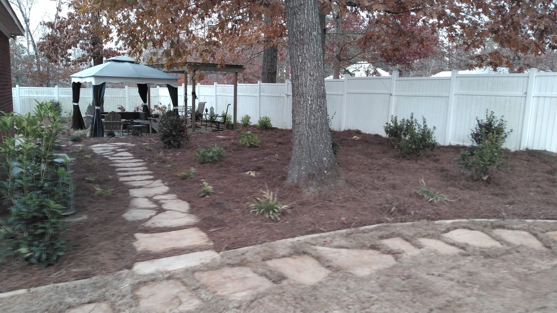 There is a gazebo in the backyard with a stone walkway leading to it.