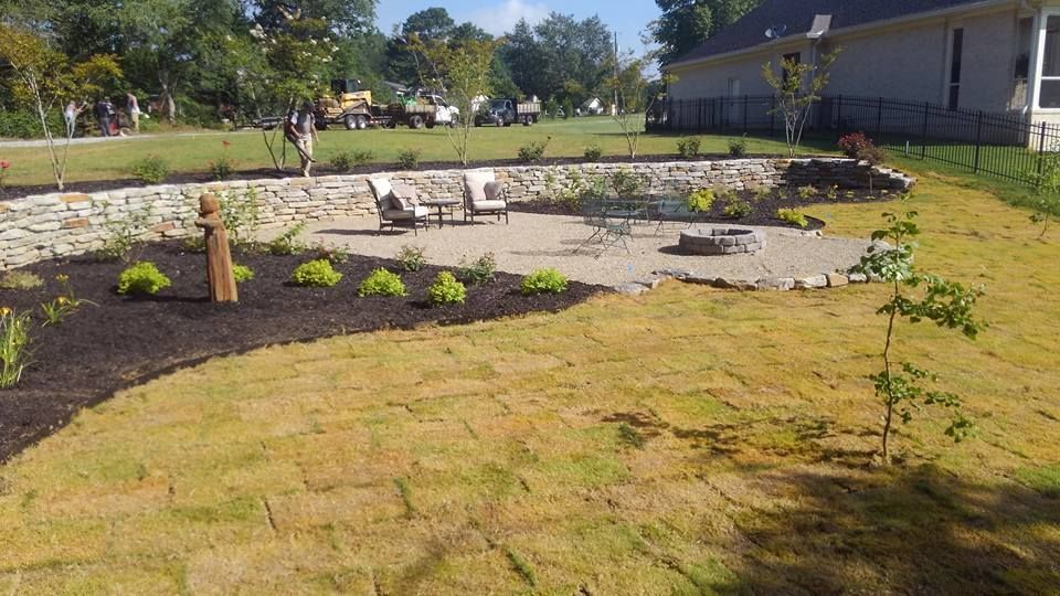 A backyard with a fire pit , chairs , and a stone wall.