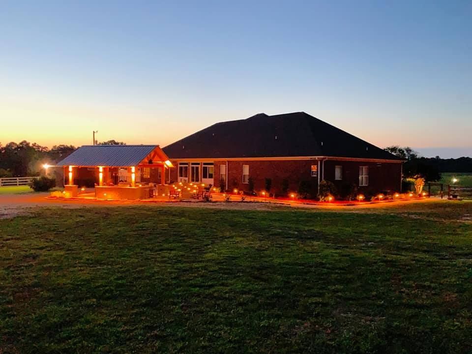 A large house is lit up at night in a grassy field.