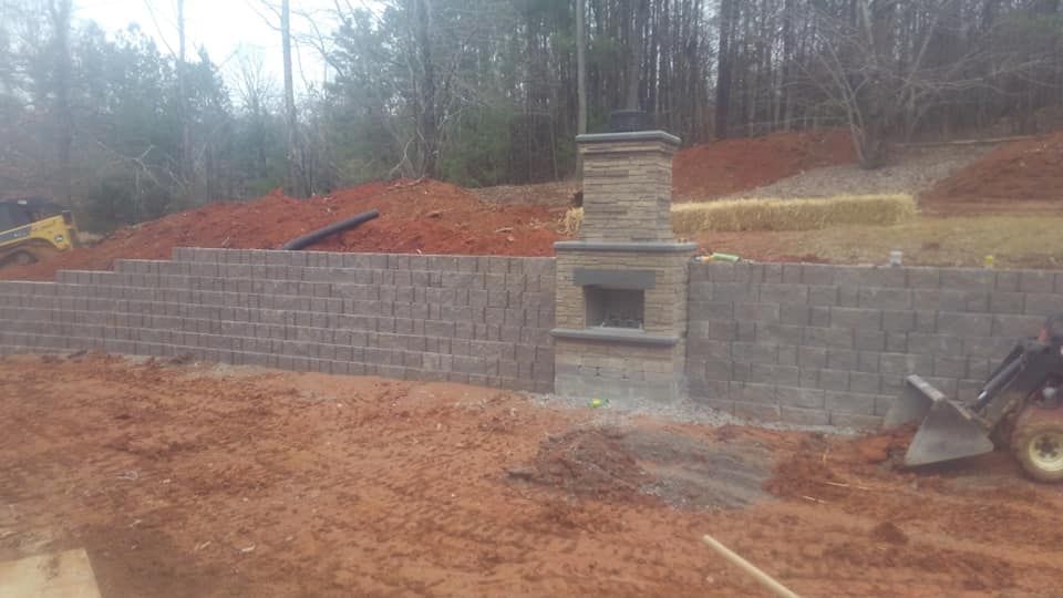 A brick wall with a fireplace in the middle of it is being built in a backyard.
