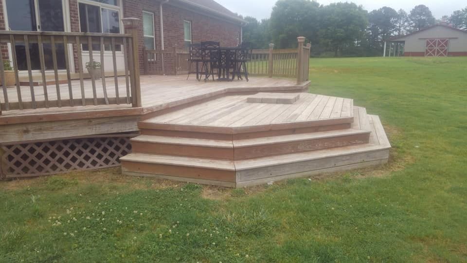 A wooden deck with stairs leading up to it is in the backyard of a house.