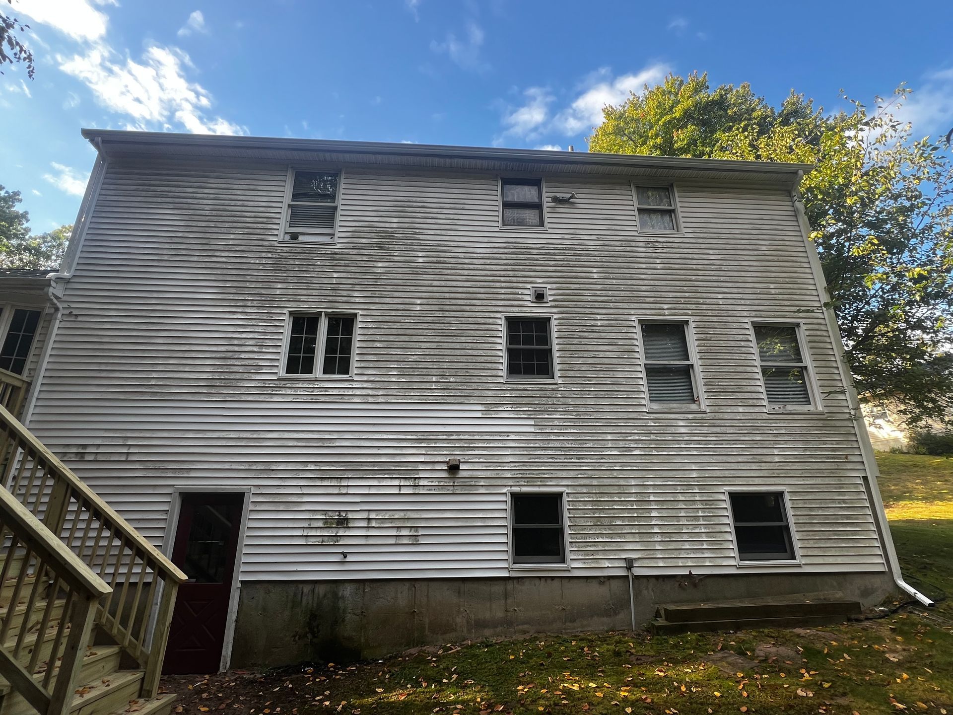 Weathered, three-story building with peeling paint and multiple windows. Wooden stairs on the left. Overcast sky.