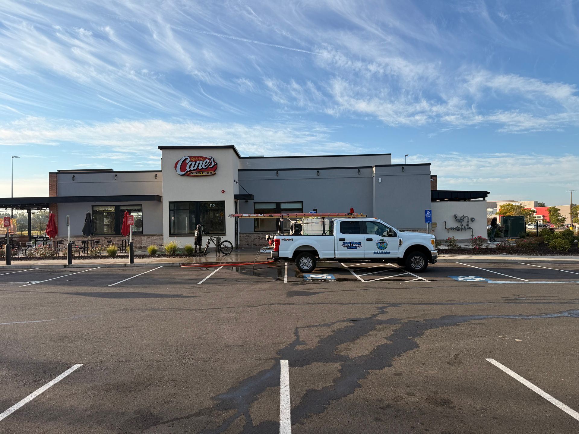 Exterior of Raising Cane's restaurant with a white work truck in the parking lot under a partly cloudy sky.