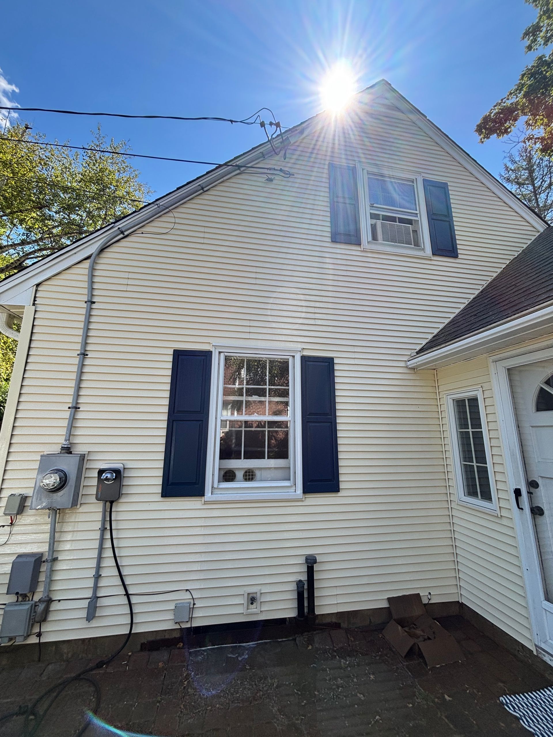 Yellow house with navy shutters, under a bright sun.