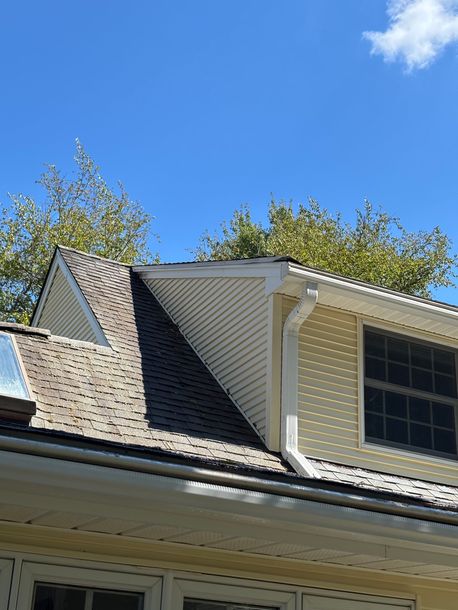 A residential house with a dark roof and yellow siding under a bright blue sky.