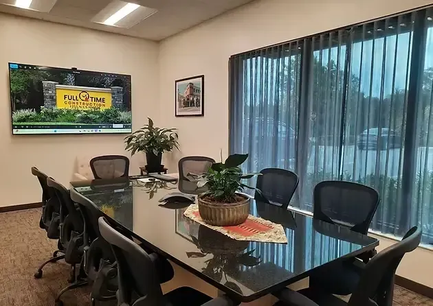 Conference room with black chairs, a long table, and a TV displaying a logo.