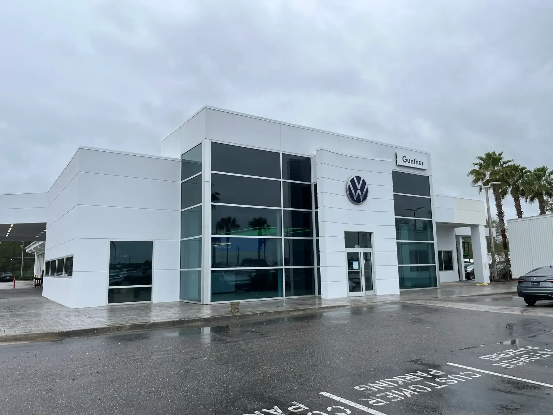 White Volkswagen dealership building with large windows and logo on a cloudy day.