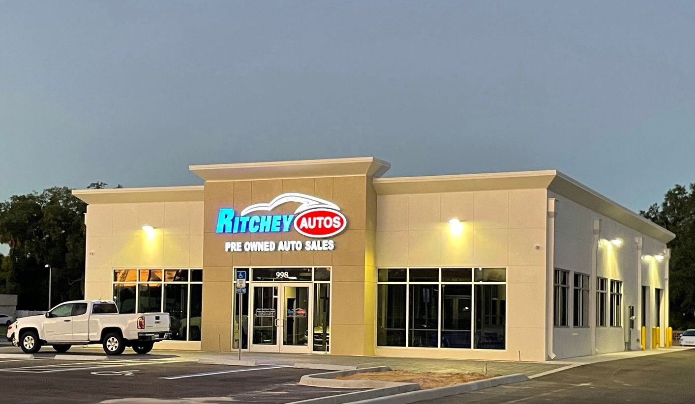 A modern Ritchey Auto sales building with large windows and a white exterior, featuring a pickup truck parked out front.