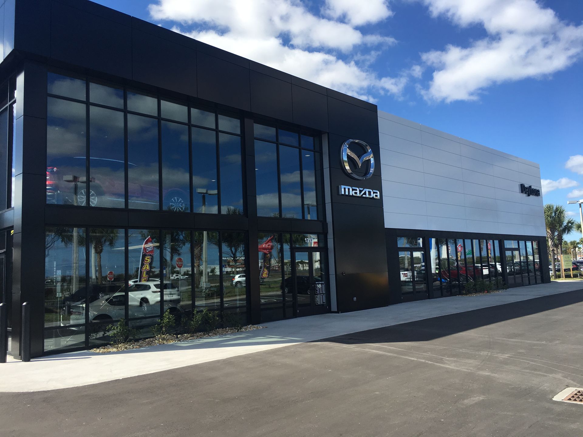 Exterior of a modern Mazda car dealership with large glass windows and a black and white facade under a blue sky.